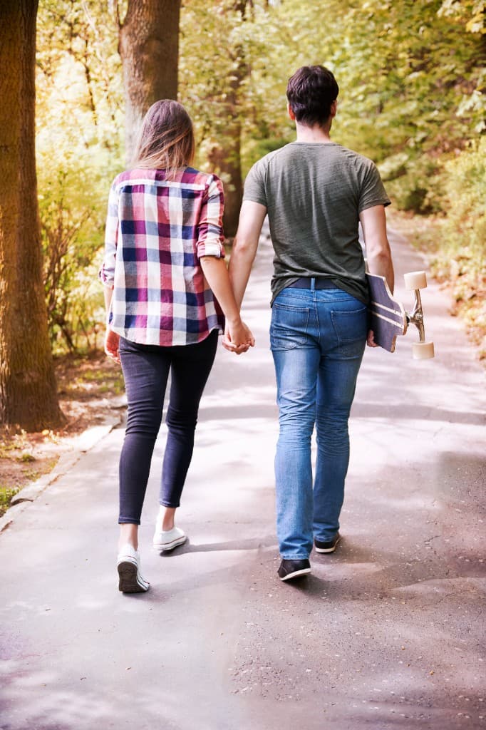 A couple walking hand in hand on a sunlit park path, bringing adventure into everyday life